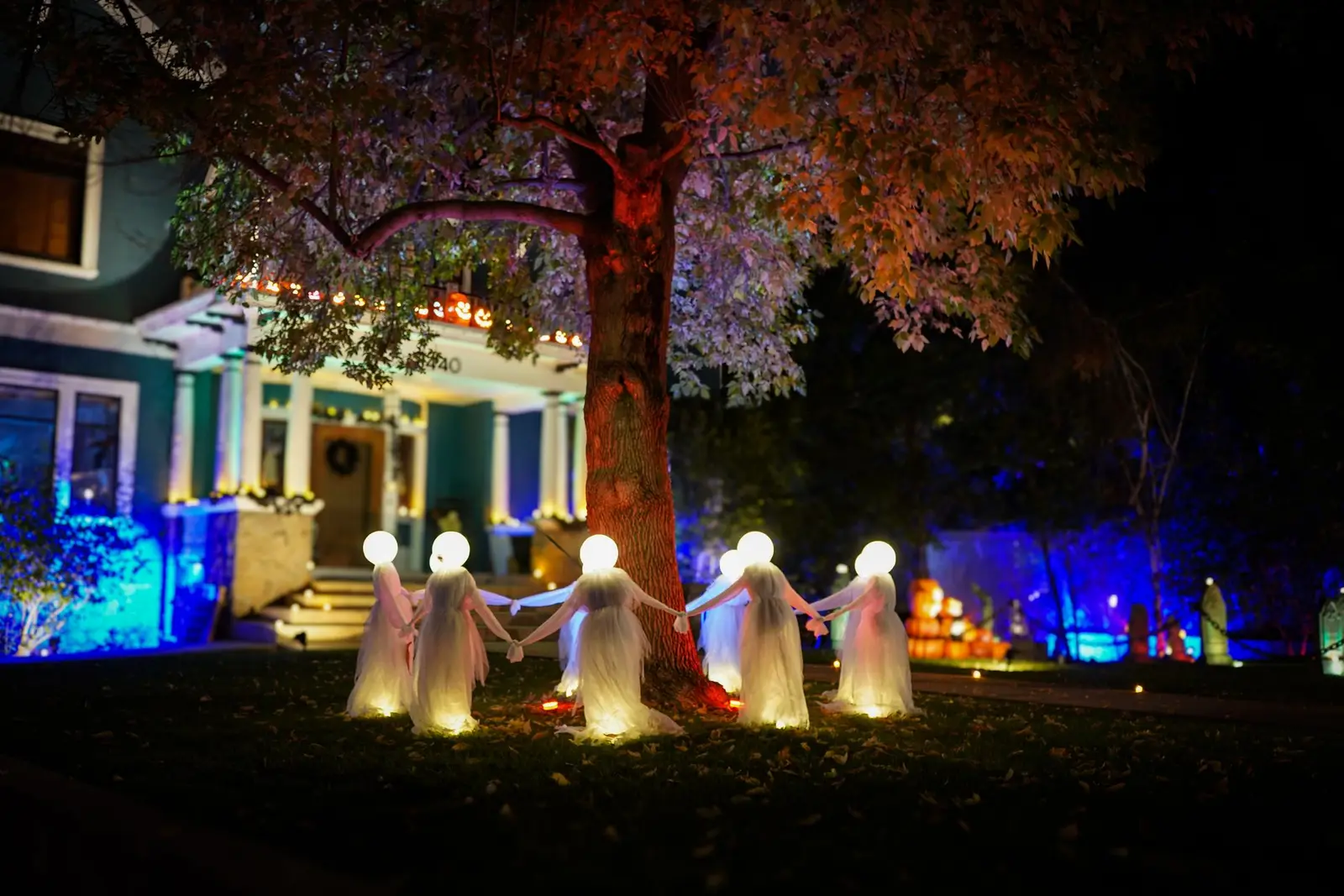 House at night with blue and green lights and glowing ghost decorations in the front yard